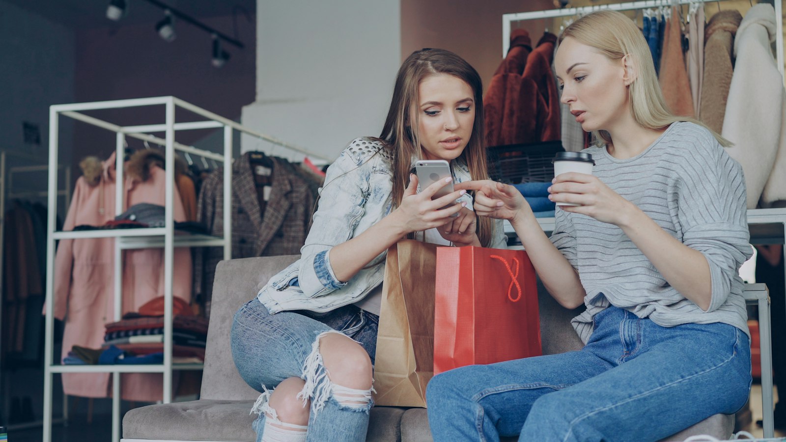 Choice overload while shopping for a new chapter Two women looking at a phone together while shopping in a clothing store